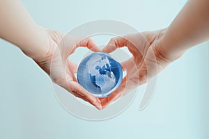 Hands in shape of heart holding blue glass globe of South and North America