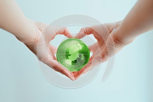 Hands in shape of heart  holding green glass globe of South Pole