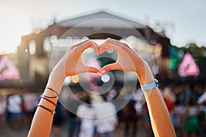 Hands shape heart sign at sunset beach music fest, crowd enjoys live concert. Outdoor summer event, happy fans party