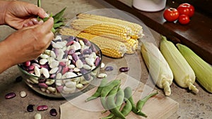 Hands shelling fresh colorful beans into glass bowl