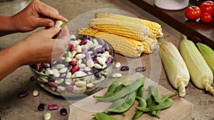 Hands shelling fresh colorful beans into glass bowl