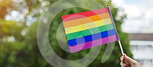 Hands showing LGBTQ Rainbow flag on green nature background. Support Lesbian, Gay, Bisexual, Transgender and Queer community and