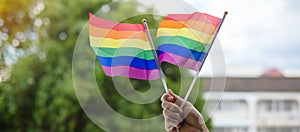 Hands showing LGBTQ Rainbow flag on green nature background. Support Lesbian, Gay, Bisexual, Transgender and Queer community and