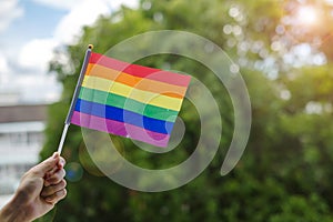 Hands showing LGBTQ Rainbow flag on green nature background. Support Lesbian, Gay, Bisexual, Transgender and Queer community and