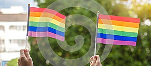 Hands showing LGBTQ Rainbow flag on green nature background. Support Lesbian, Gay, Bisexual, Transgender and Queer community and