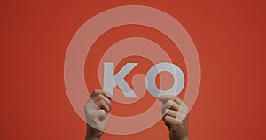 Hands showing word KO of english language. Man shows knockout sign made of carved paper for blog