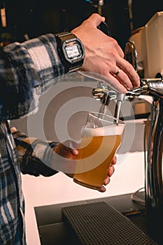 Hands of skilled bartender pouring unfiltered craft beer from tap into glass