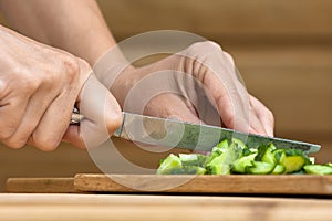 Hands slicing cucumber on the wooden cutting board