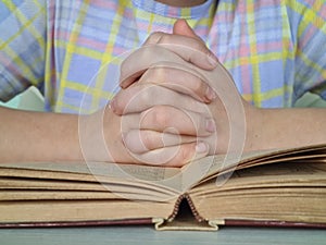 Hands of small Christian child are folded in prayer over book of Bible