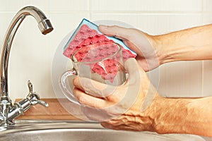 Hands with sponge and dirty cup over the sink in kitchen