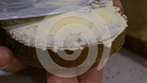 Hands Spreading Butter with a knife on Dark Bread Slice, extreme close-up view