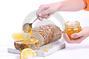 Hands sprinkle jam on biscuit roll. Sponge cake with orange jam on a white wooden background.