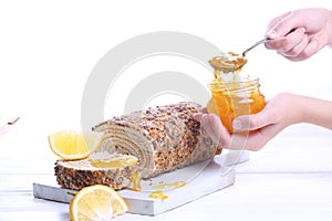 Hands sprinkle jam on biscuit roll. Sponge cake with orange jam on a white wooden background.