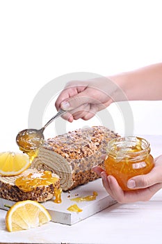 Hands sprinkle jam on biscuit roll. Sponge cake with orange jam on a white wooden background.