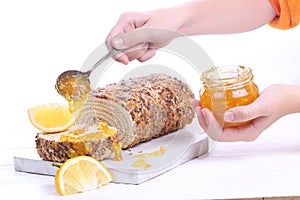 Hands sprinkle jam on biscuit roll. Sponge cake with orange jam on a white wooden background.