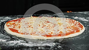 Hands are sprinkling fresh grated cheese on pizza dough, close up. Chef is cooking pizza. Process of preparing traditional italian