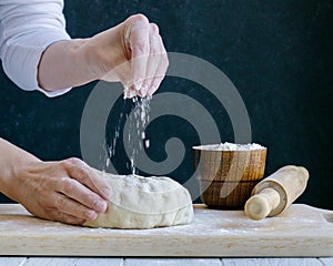 Hands sprinkling white wheat flour over piece of raw dough