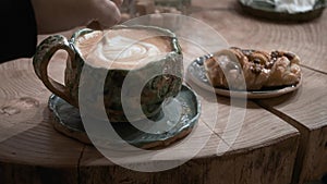 Hands stir coffee in green mug with teaspoon at cafe. sweet bun on background