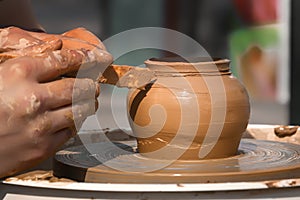 Hands of a street potter make a clay pot on a potter`s wheel.