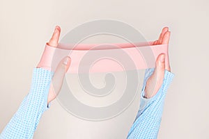 Hands stretching a pink fitness elastic band on gray background close-up.