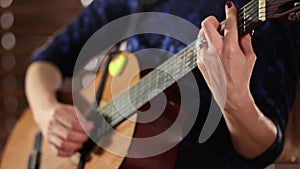 Hands on the strings of an acoustic guitar. Close-up. A girl in a blue dress is playing a musical instrument. Defocus at the begin