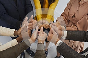 Hands of successful multiracial business team standing in circle and showing thumbs up.