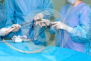 Hands of surgeons in sterile gloves use laparoscopic surgical instruments.