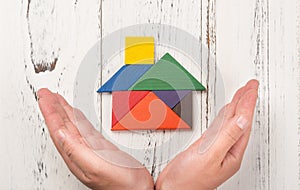 Hands surround a wooden house made by tangram home insurance concept or representing home owner ship