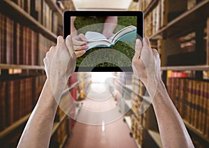Hands with tablet showing book against grass against bookshelves