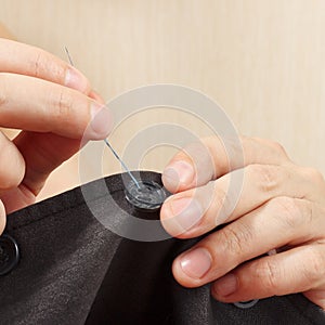 Hands of tailor sew a button to gray jacket close up