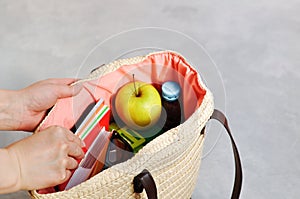 Hands take the Stylish fashionable wicker bag with textbooks and notebooks, lunchbox and green Apple, water for a snack