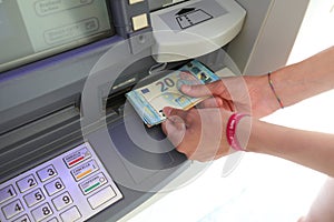 hands taking 20 Euro bills from an ATM machine after typing the