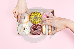 Hands is taking colored glazed donuts in donut box. Hands is grabbing different flavors doughnuts. Unhealthy snack in the office