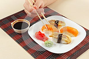 Hands taking ginger with chopsticks. Sushi with omelet with eel and with salmon and ginger and wasabi on black and red bamboo mat