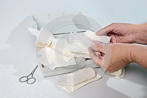 Hands taking out a bandage from a first aid kit with medical supplies, health and medicine concept, light gray background, copy