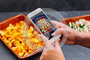 Hands taking photo baked potatoes in a casserole with smartphone