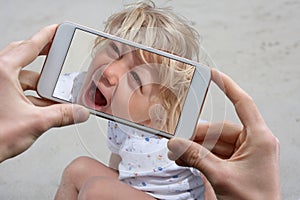 Hands taking a photo with a mobile phone of a laughing little child in summer holidays