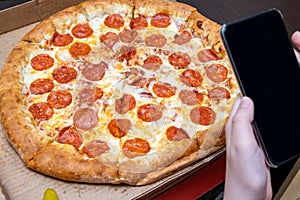 Hands taking photos of hot delicious italian pepperoni pizza using smartphone