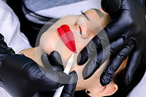 The hands of the tattoo master in black gloves hold a white pencil and outline the contour of the lips painted with a red pencil