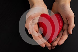 Hands of a teenager child holding a red wooden heart in their hands