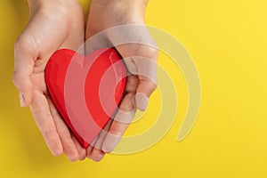 Hands of a teenager child holding a red wooden heart in their hands