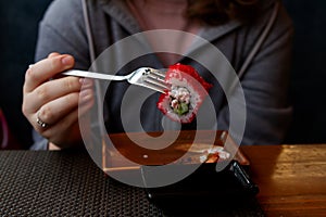 The hands of a teenager in a gray hoodie are holding sushi food with a European device with an iron fork