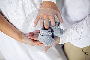 Hands of their parents, dressed in white, holding a knitted blue booties