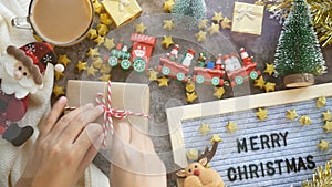 Hands tie a bow in a rope on kraft paper sheets for Christmas gift box present on a table with Christmas ornaments decoration