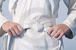 Hands tightening white belt on a teenage dressed in kimono