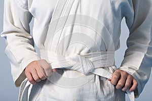 Hands tightening white belt on a teenage dressed in kimono