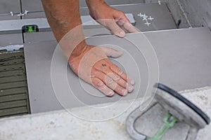 The hands of the tiler are laying the ceramic tile on the floor.