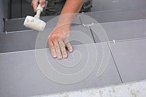 The hands of the tiler are laying the ceramic tile on the floor.