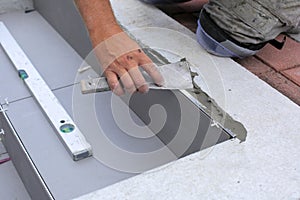 The hands of the tiler are laying the ceramic tile on the floor.