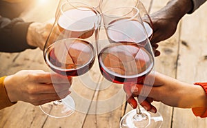 Hands toasting red wine glass and friends having fun cheering at winetasting experience - Young people enjoying time together at